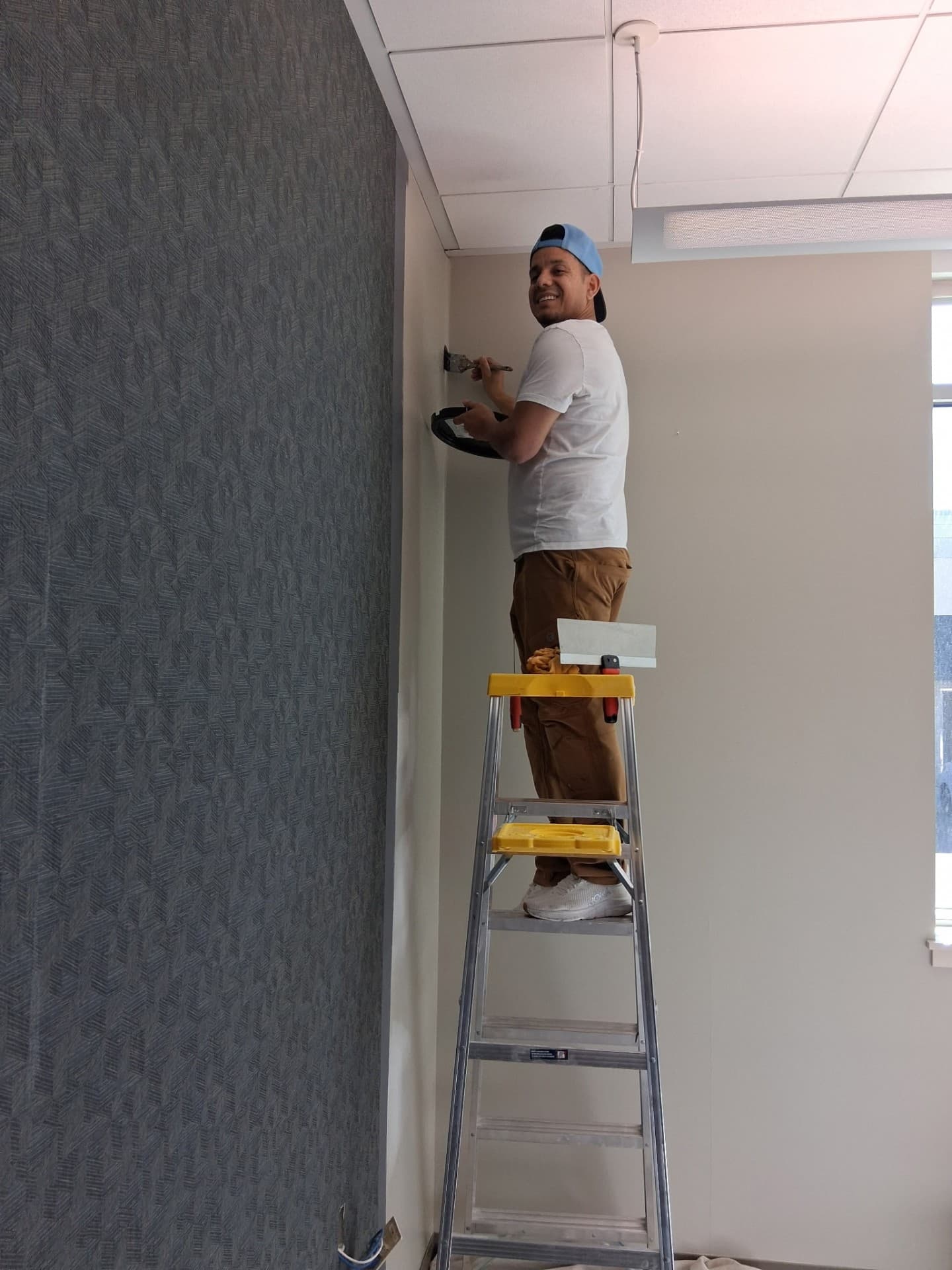 Wallpaper Deluxe installer on a ladder smoothing a freshly-hung panel