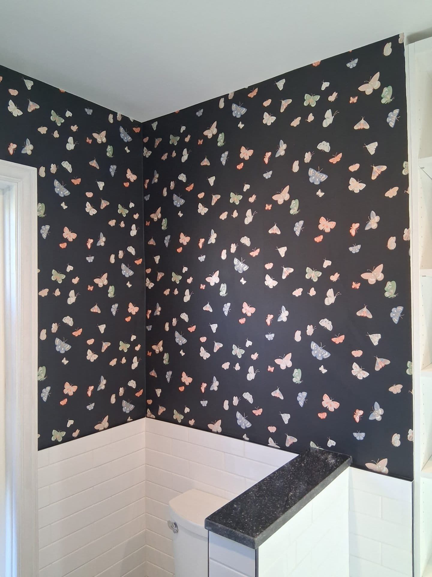 Bathroom with navy butterfly wallpaper above white wainscoting