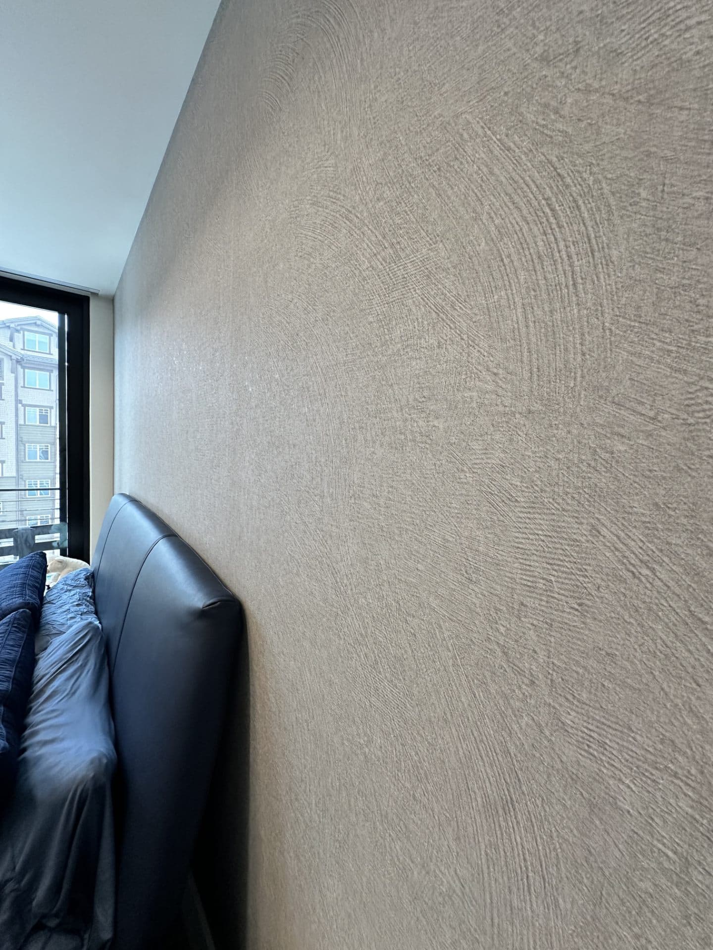 Bedroom with a black bed framed against a city view and wallpapered wall