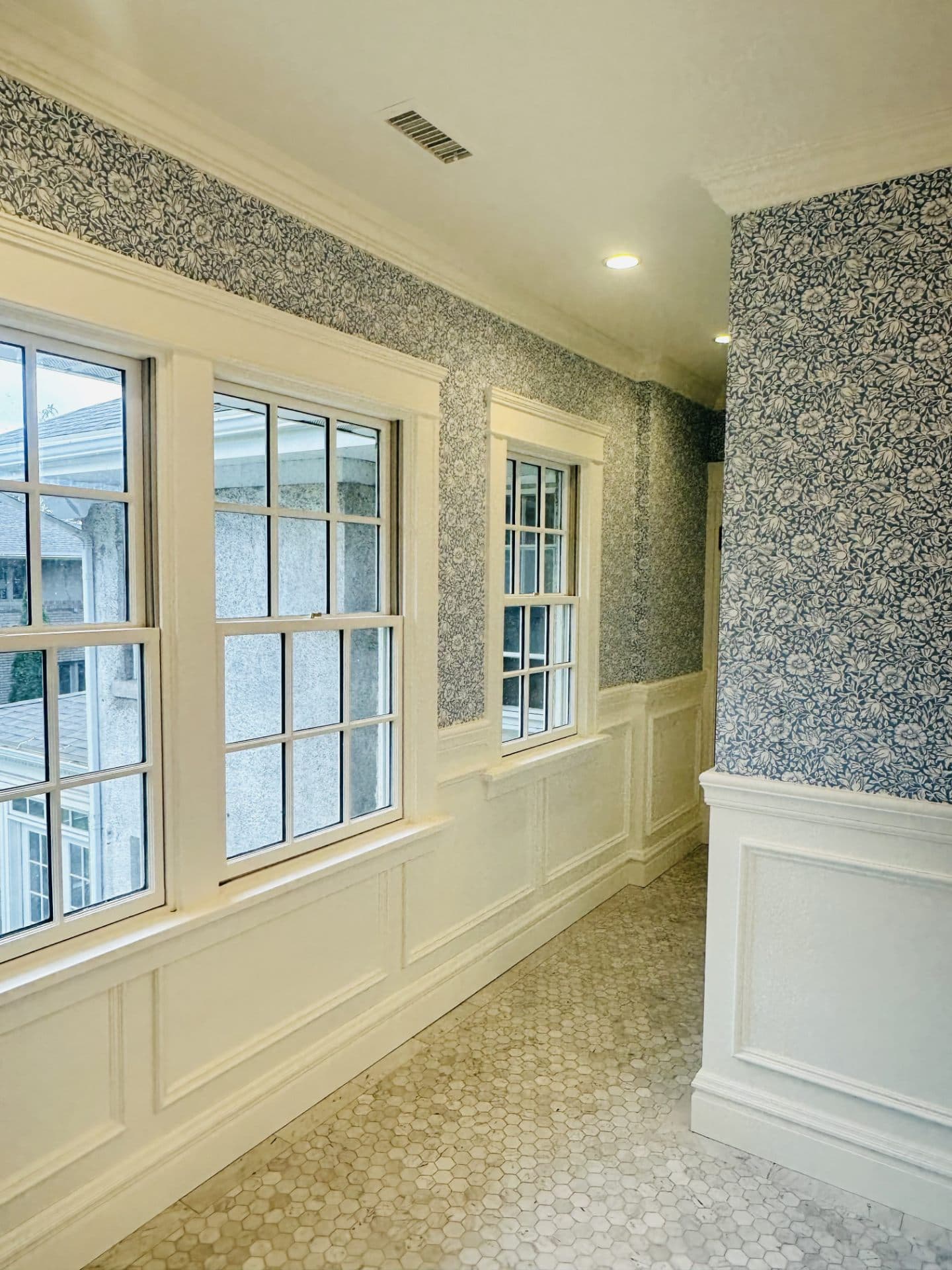 Hallway with patterned wallpaper, wainscoting, and tile flooring