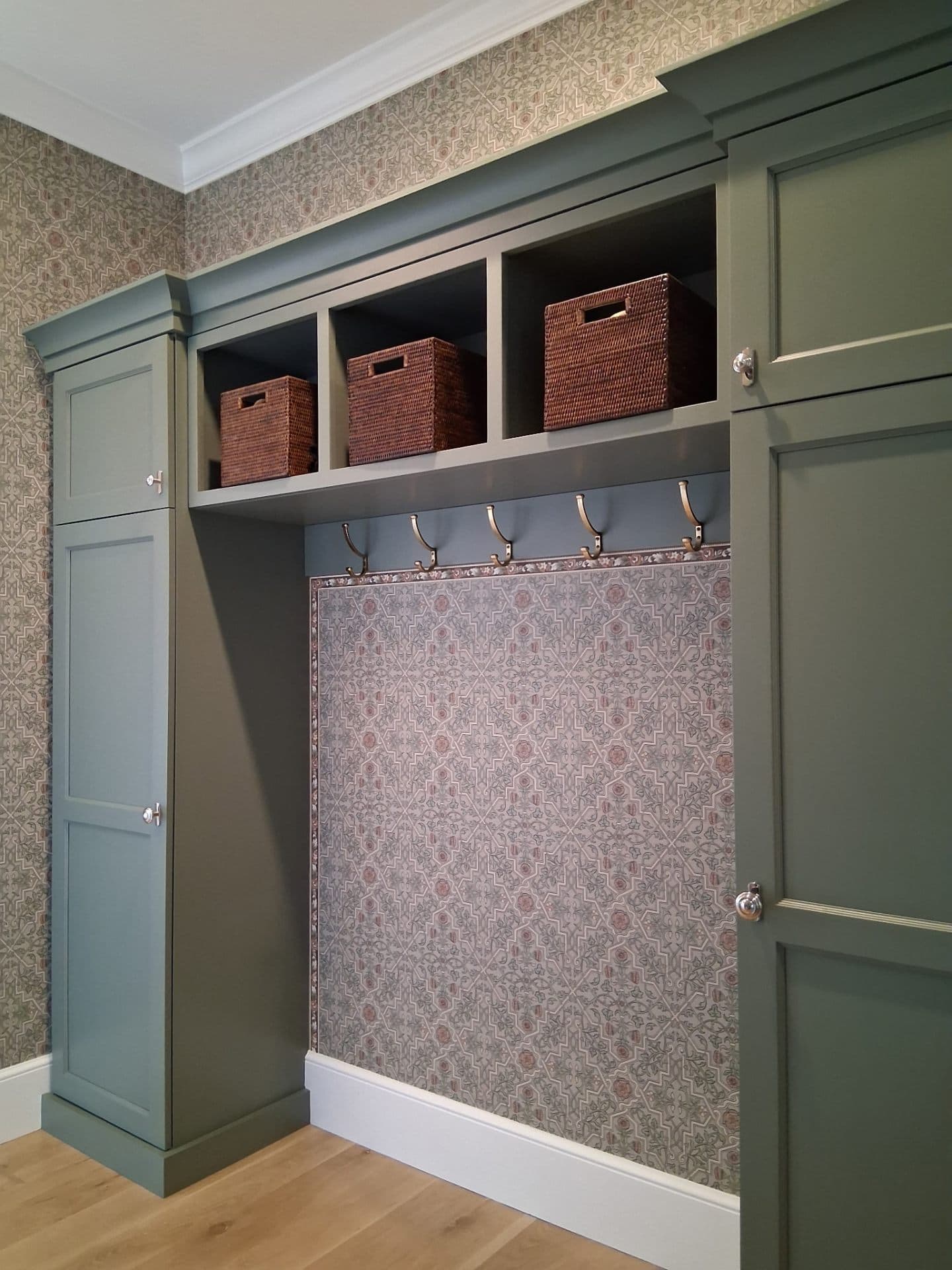 Mudroom with sage green cabinetry, wicker baskets, and patterned wall
