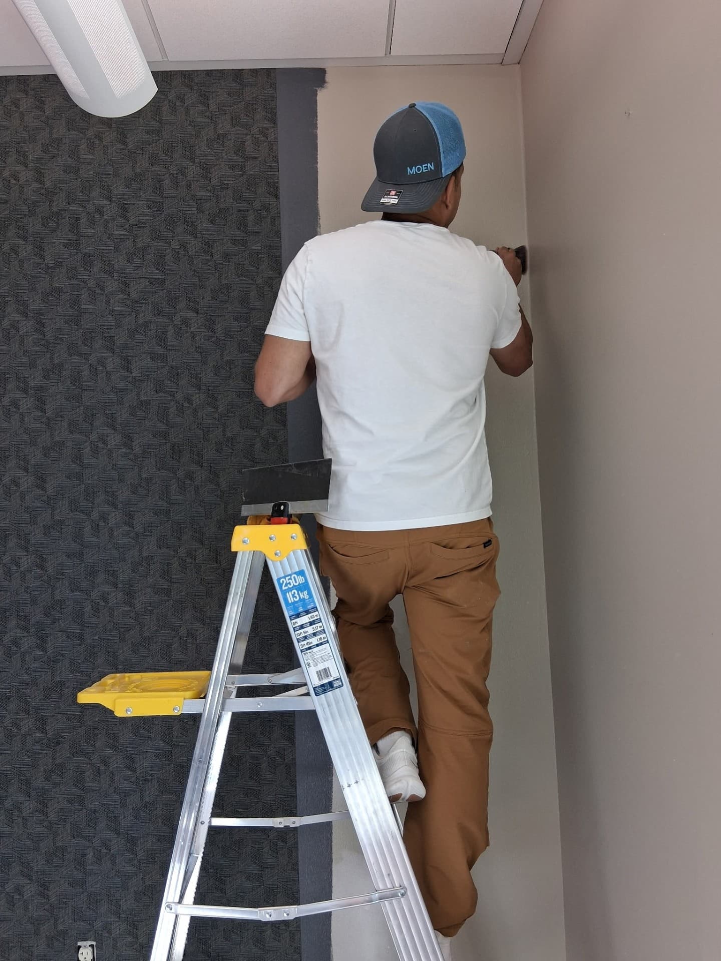 Installer on a ladder hanging the next drop of wallpaper