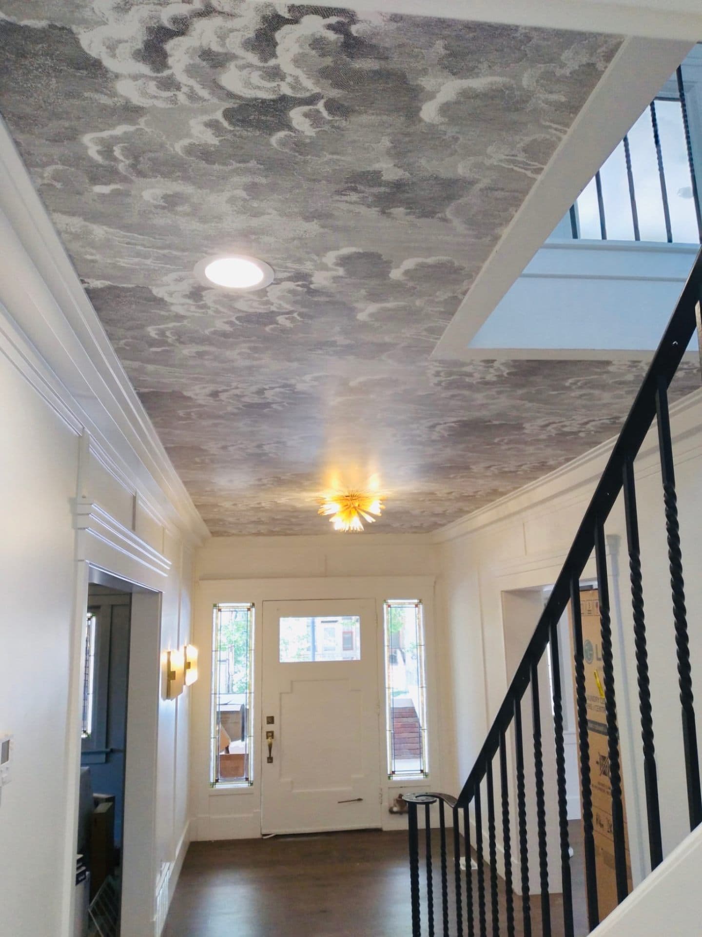 Foyer with patterned wallpaper on the ceiling above a hardwood staircase